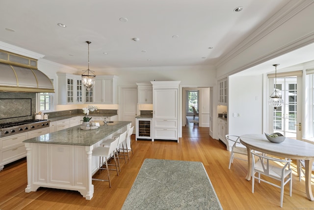 kitchen featuring stainless steel gas stovetop, an inviting chandelier, white cabinetry, beverage cooler, and a center island