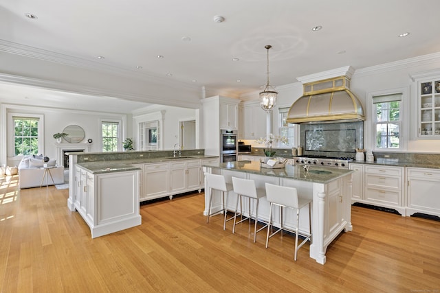 kitchen featuring pendant lighting, custom exhaust hood, sink, white cabinetry, and light wood-type flooring