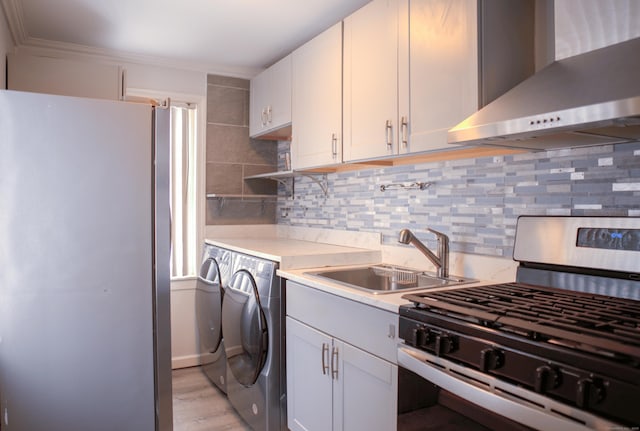 kitchen featuring appliances with stainless steel finishes, wall chimney exhaust hood, sink, white cabinetry, and separate washer and dryer