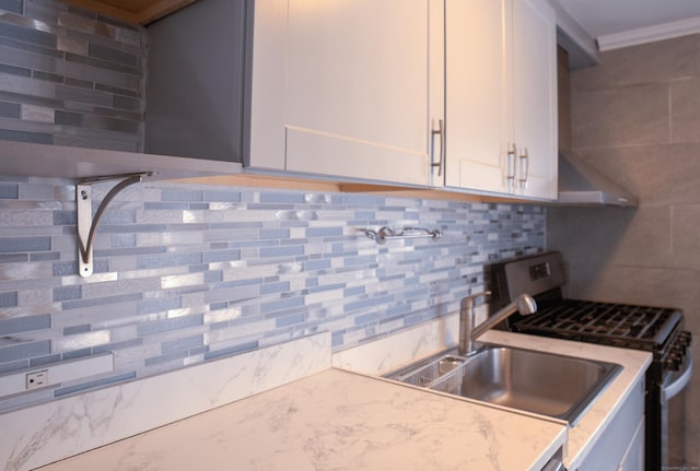 kitchen featuring gas range, sink, white cabinetry, light stone counters, and decorative backsplash