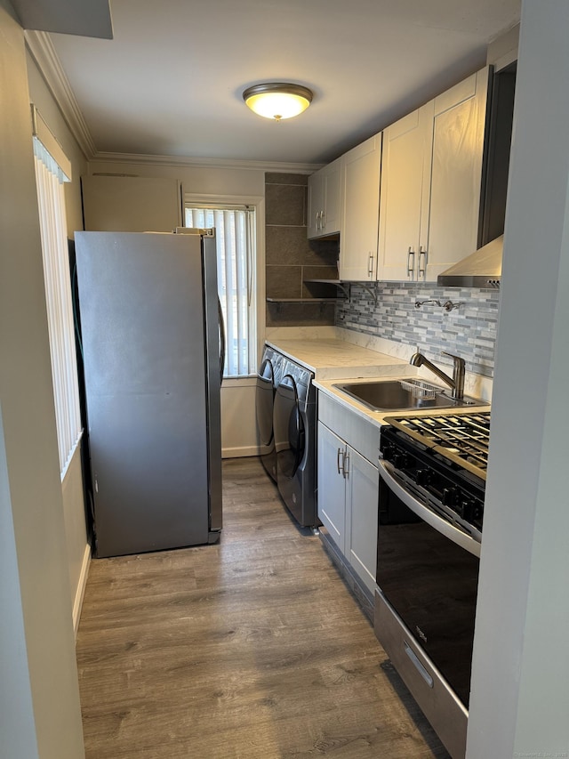 kitchen with appliances with stainless steel finishes, sink, backsplash, white cabinetry, and washing machine and dryer