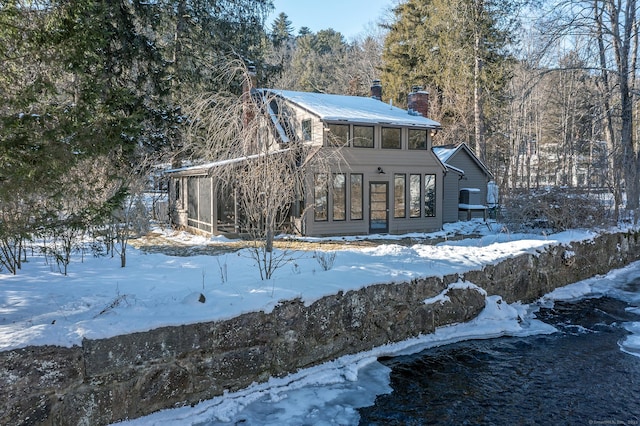 snow covered rear of property with a sunroom