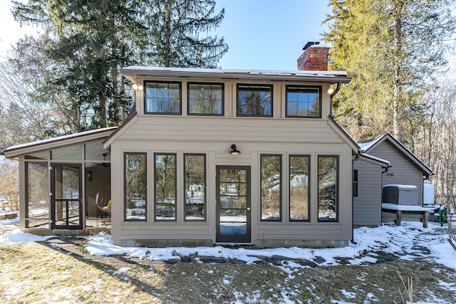 snow covered back of property with a sunroom