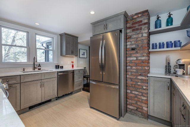 kitchen with sink, gray cabinets, appliances with stainless steel finishes, light stone countertops, and light hardwood / wood-style floors