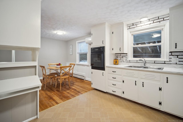 kitchen with sink, white cabinetry, oven, a textured ceiling, and an AC wall unit