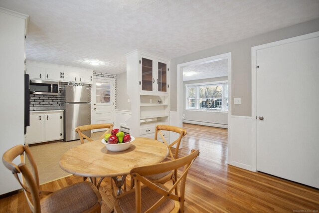 dining room with light hardwood / wood-style flooring, a baseboard radiator, and a textured ceiling