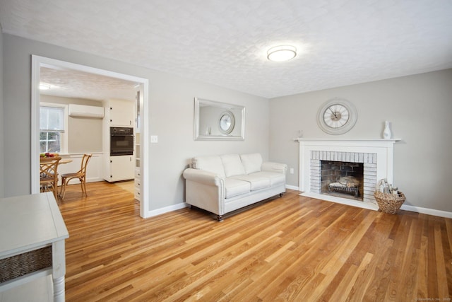 living room featuring a fireplace, a wall mounted AC, a textured ceiling, and light wood-type flooring