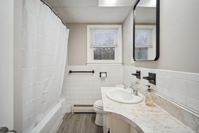 full bathroom featuring a paneled ceiling, wood-type flooring, tile walls, vanity, and a baseboard heating unit