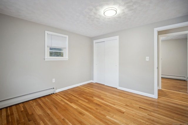 unfurnished bedroom featuring a baseboard radiator, wood-type flooring, a closet, and a textured ceiling