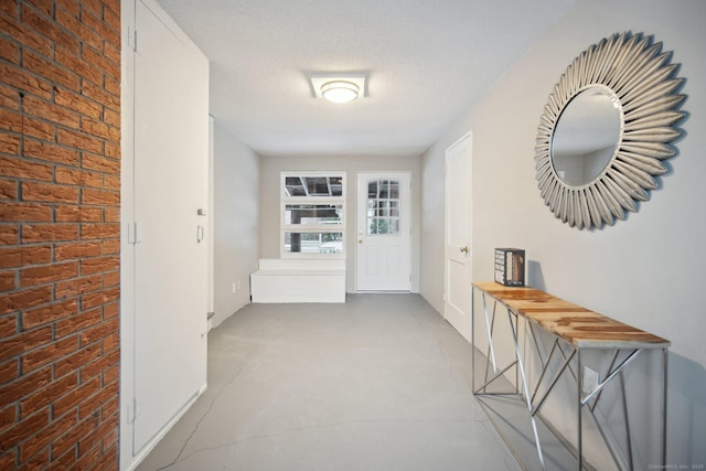 corridor featuring a textured ceiling and brick wall