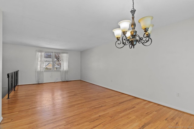 empty room with light wood-type flooring and a notable chandelier