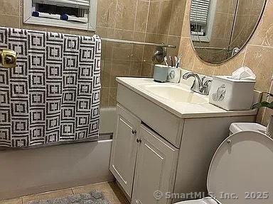 full bathroom with toilet, shower / bath combo with shower curtain, tile walls, tile patterned floors, and vanity