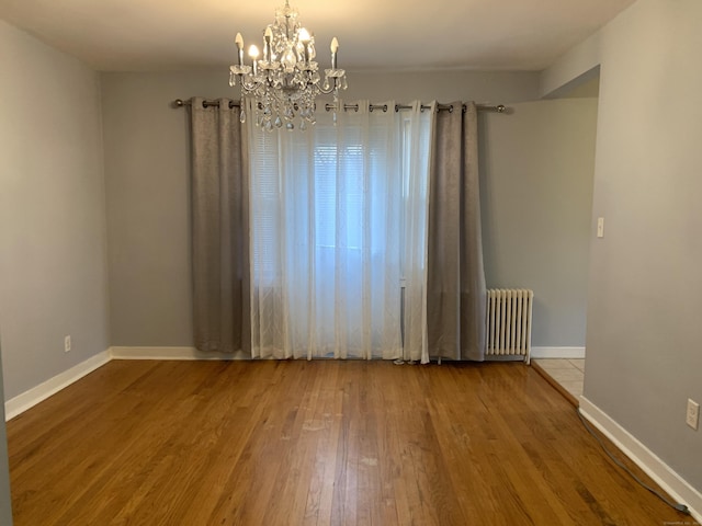 empty room featuring a notable chandelier, radiator heating unit, and hardwood / wood-style floors