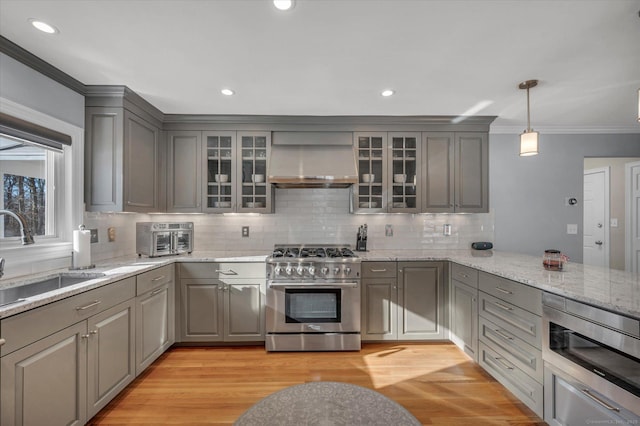 kitchen featuring sink, decorative light fixtures, gray cabinets, stainless steel appliances, and wall chimney range hood