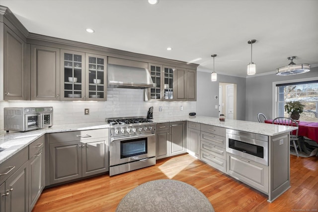 kitchen featuring gray cabinetry, decorative light fixtures, appliances with stainless steel finishes, kitchen peninsula, and wall chimney range hood