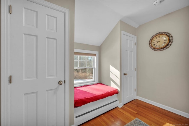 bedroom with a baseboard radiator, wood-type flooring, and vaulted ceiling