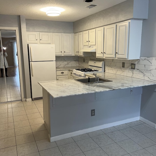 kitchen with kitchen peninsula, white appliances, white cabinets, light stone counters, and sink