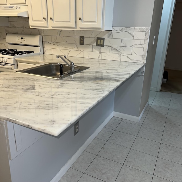 kitchen featuring white gas range oven, sink, light tile patterned floors, light stone countertops, and white cabinets