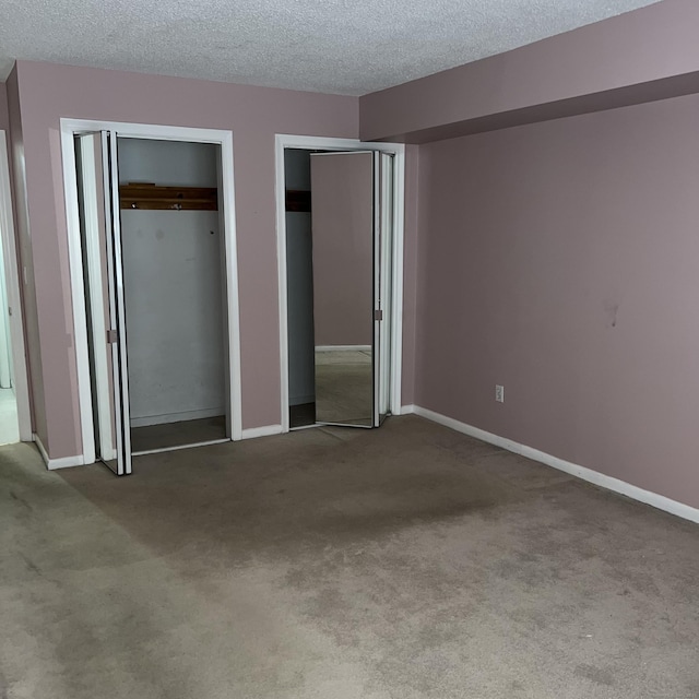 unfurnished bedroom with two closets, a textured ceiling, and light carpet