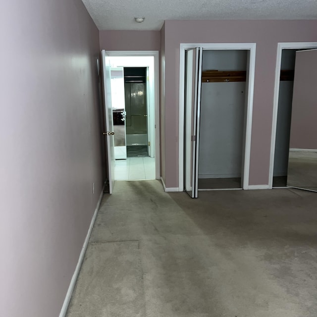 interior space featuring light colored carpet, a textured ceiling, and multiple closets