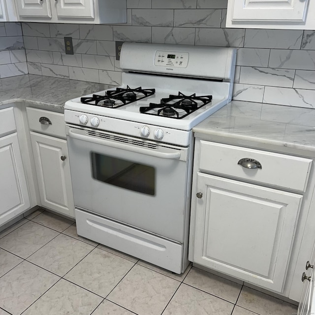 kitchen with light tile patterned floors, white cabinetry, tasteful backsplash, and white gas range oven