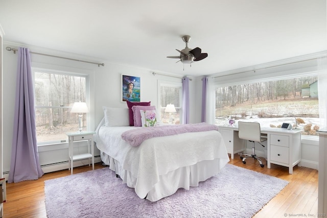 bedroom with baseboard heating, built in desk, light hardwood / wood-style floors, ornamental molding, and ceiling fan