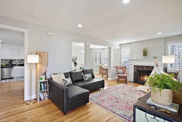 living room featuring a wealth of natural light, light hardwood / wood-style flooring, and a stone fireplace