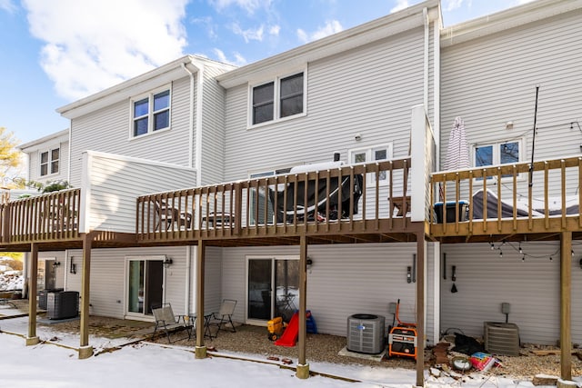 snow covered back of property with cooling unit and a deck