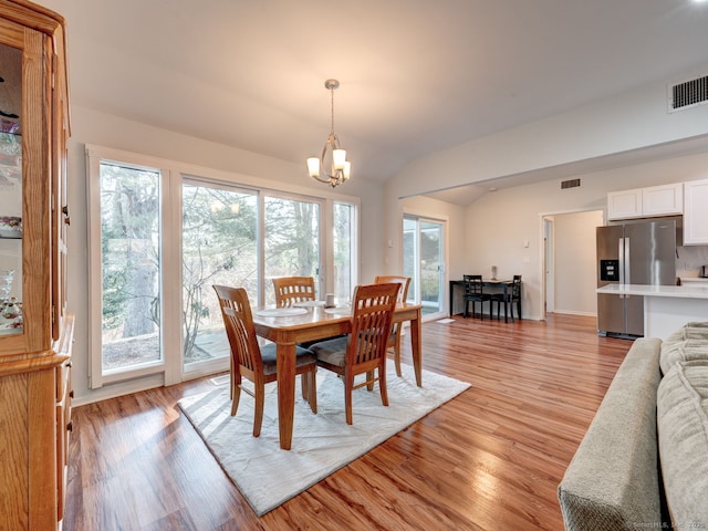 dining space with visible vents, a notable chandelier, light wood-style flooring, and vaulted ceiling