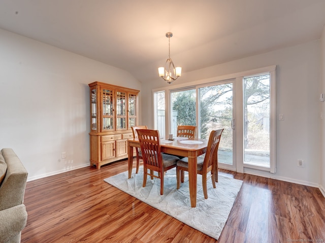 dining area featuring a chandelier, vaulted ceiling, baseboards, and wood finished floors