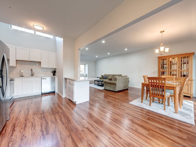 kitchen featuring open floor plan, dishwasher, light countertops, light wood-style flooring, and an inviting chandelier