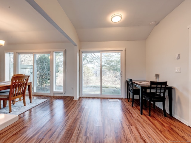 dining room with a wealth of natural light, vaulted ceiling, and wood finished floors