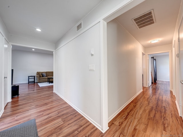 hallway with light wood finished floors, visible vents, and baseboards