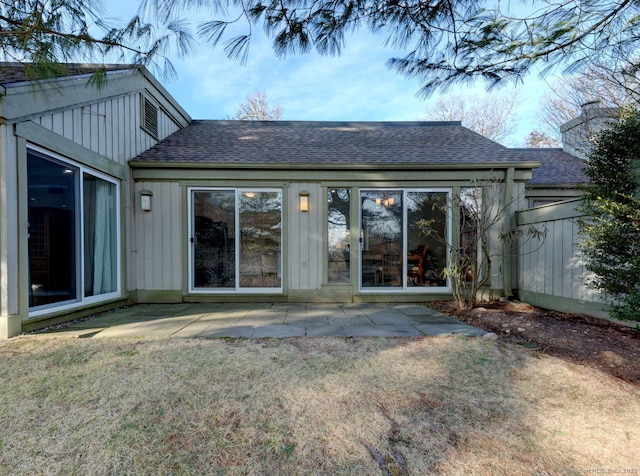 back of property featuring a patio, a lawn, roof with shingles, and a chimney