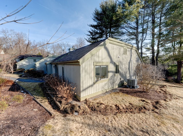 view of side of home featuring central AC and a shingled roof