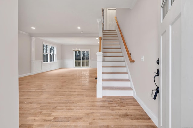 entryway with crown molding, light hardwood / wood-style floors, and an inviting chandelier