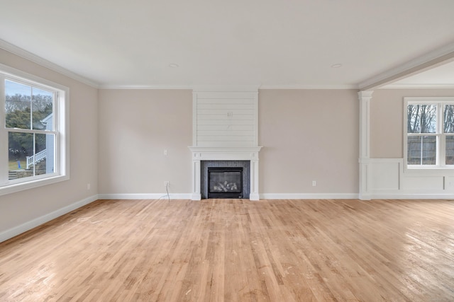 unfurnished living room with light hardwood / wood-style flooring, ornamental molding, ornate columns, and a fireplace