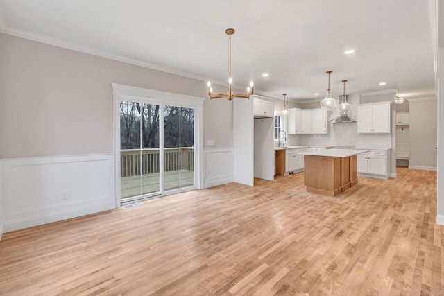 kitchen featuring a kitchen island, white cabinetry, sink, hanging light fixtures, and crown molding