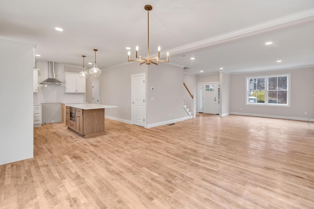 kitchen featuring hanging light fixtures, a large island, wall chimney range hood, white cabinets, and ornamental molding