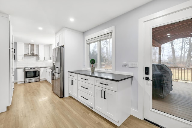 kitchen featuring white cabinets, light wood-type flooring, wall chimney exhaust hood, and appliances with stainless steel finishes