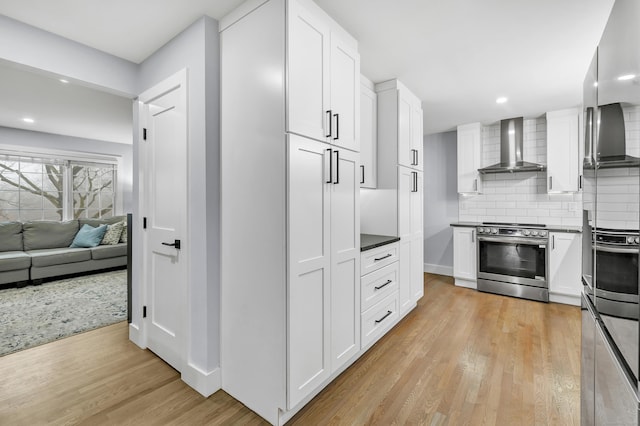 kitchen with white cabinetry, appliances with stainless steel finishes, wall chimney range hood, and backsplash