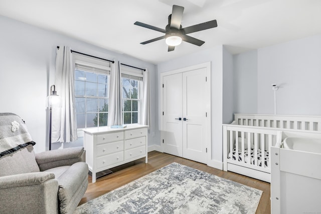 bedroom with a nursery area, hardwood / wood-style floors, ceiling fan, and a closet