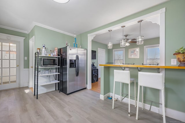 kitchen featuring appliances with stainless steel finishes, decorative light fixtures, a breakfast bar area, light hardwood / wood-style floors, and kitchen peninsula