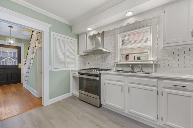 kitchen featuring decorative light fixtures, sink, white cabinets, stainless steel range with gas stovetop, and wall chimney exhaust hood