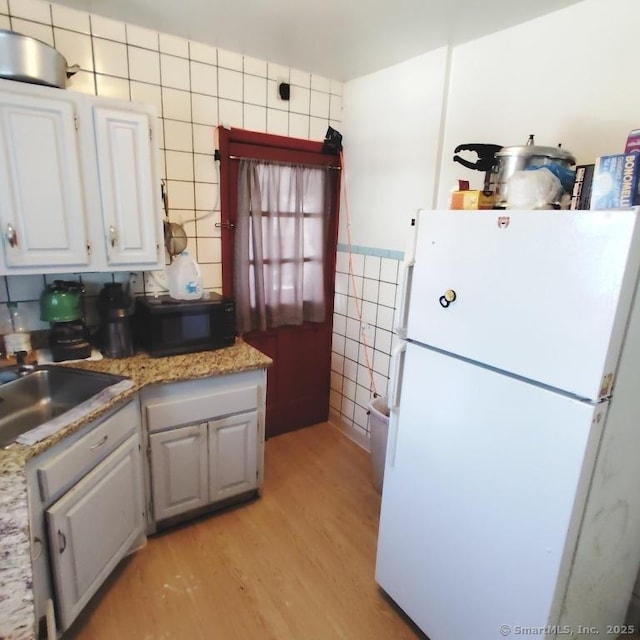 kitchen featuring light hardwood / wood-style floors, white cabinetry, tile walls, white fridge, and sink