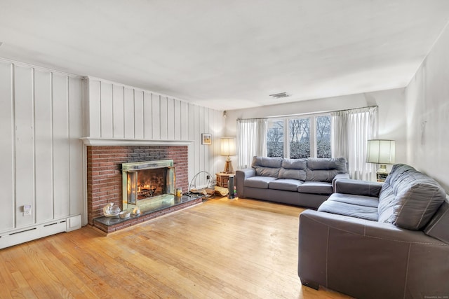 living room featuring light hardwood / wood-style flooring, a brick fireplace, and a baseboard radiator