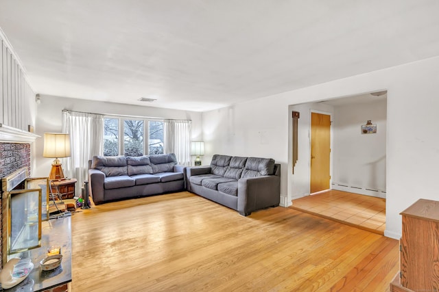 living room featuring light hardwood / wood-style floors, a tile fireplace, and a baseboard radiator