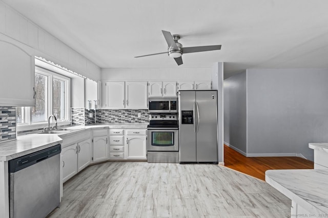 kitchen with tasteful backsplash, white cabinetry, sink, stainless steel appliances, and light wood-type flooring