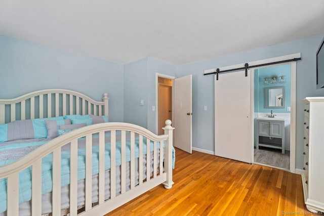 bedroom featuring ensuite bath, a barn door, and light hardwood / wood-style flooring