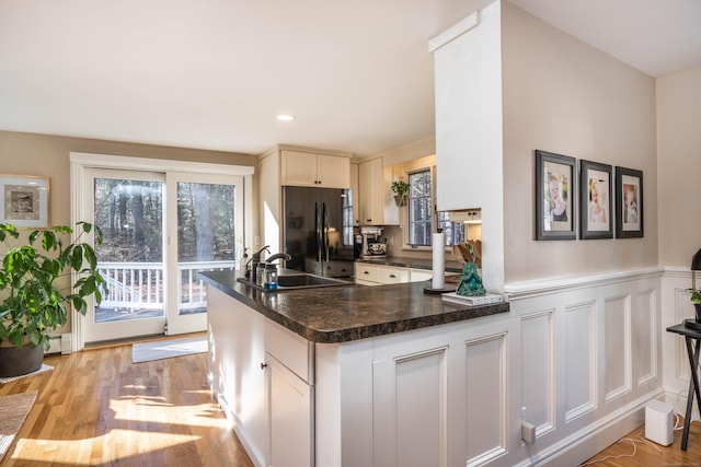 kitchen featuring white cabinetry, black fridge, kitchen peninsula, and light wood-type flooring